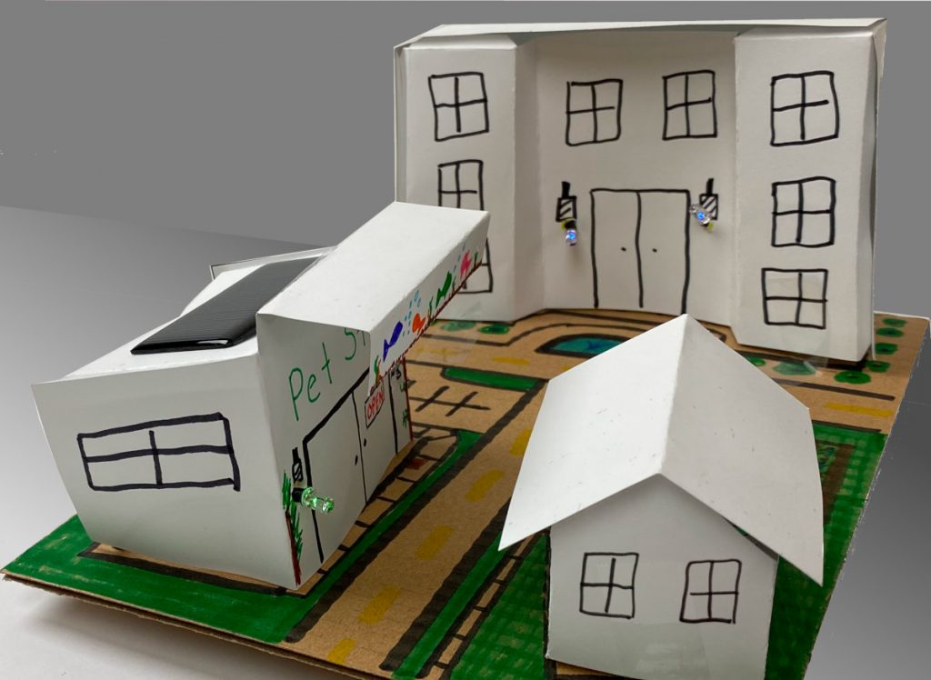 Assembled Solar Community Kit with a pet store, apartment building, and home, each lit by LEDs through a solar panel.